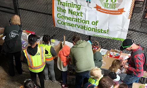 A group of families interact with games in front of a sign that reads "Training the Next Generation of Conservationists!"
