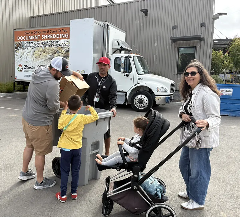 A family empties a box into the MSS Shredding Cart at Customer Appreciation Day 2026