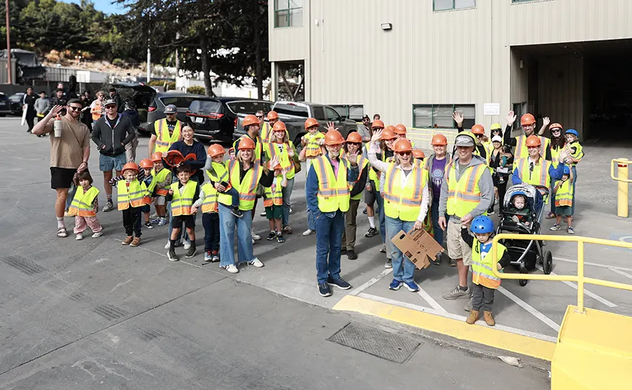 A group in hard hats and orange vests tours the Recycling Facility
